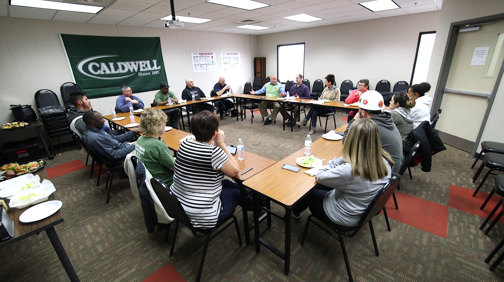 group meeting at square table in front of caldwell logo